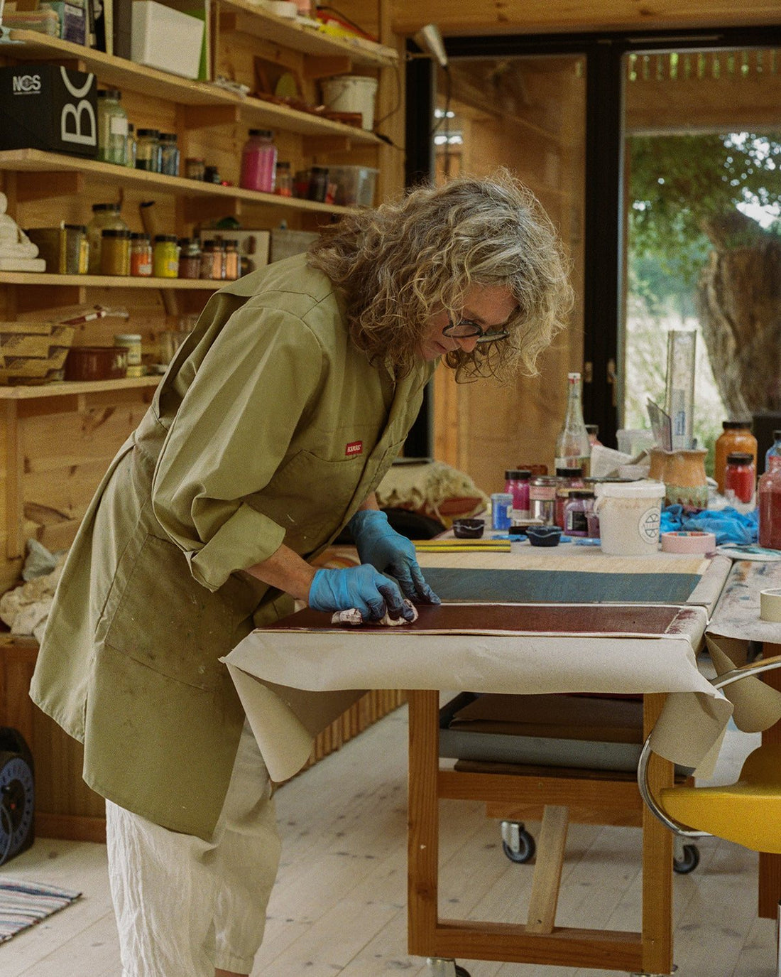 Malene Bach colouring at her worktable in the studio, shelves of pigment jars behind (Artisan Edition for FRAMA).