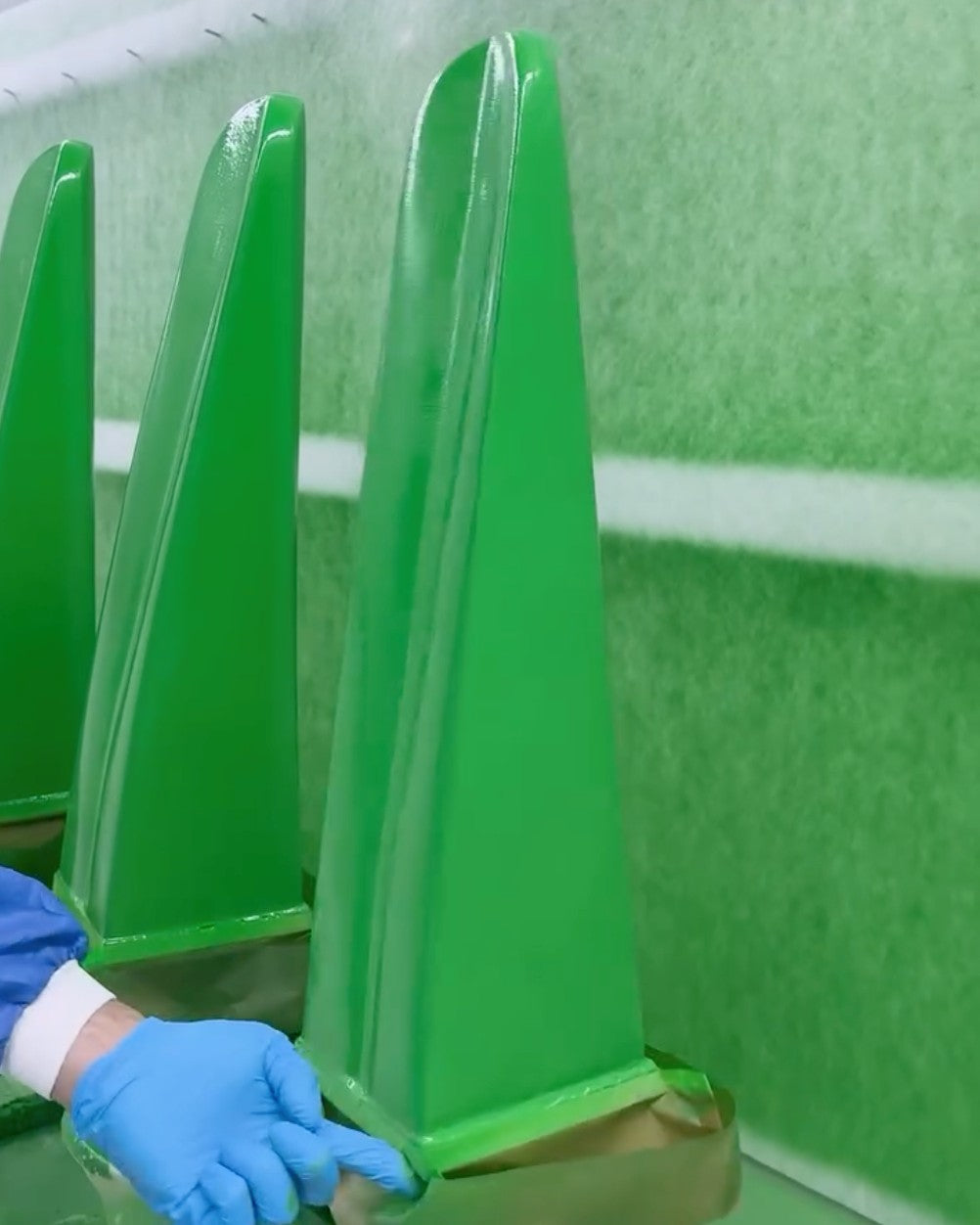 A gloved hand steadies freshly lacquered green pieces in the Gufram spray booth