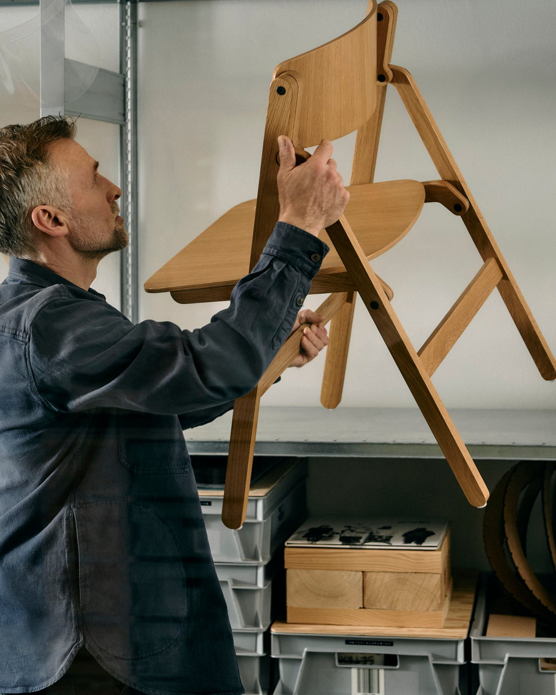 Designer Gudmundur Ludvik lifts a wooden Backflip folding chair from a workshop shelf