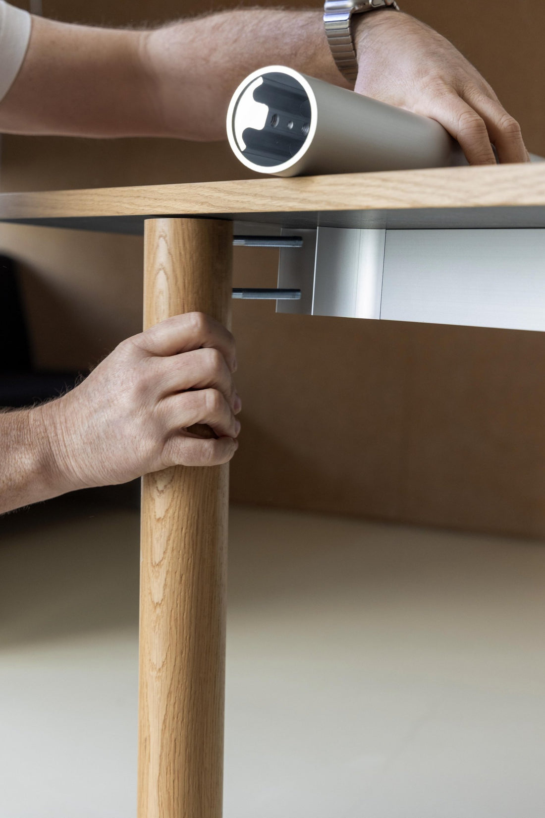 Hands fixing a solid wood leg to the underside of a table during prototyping.