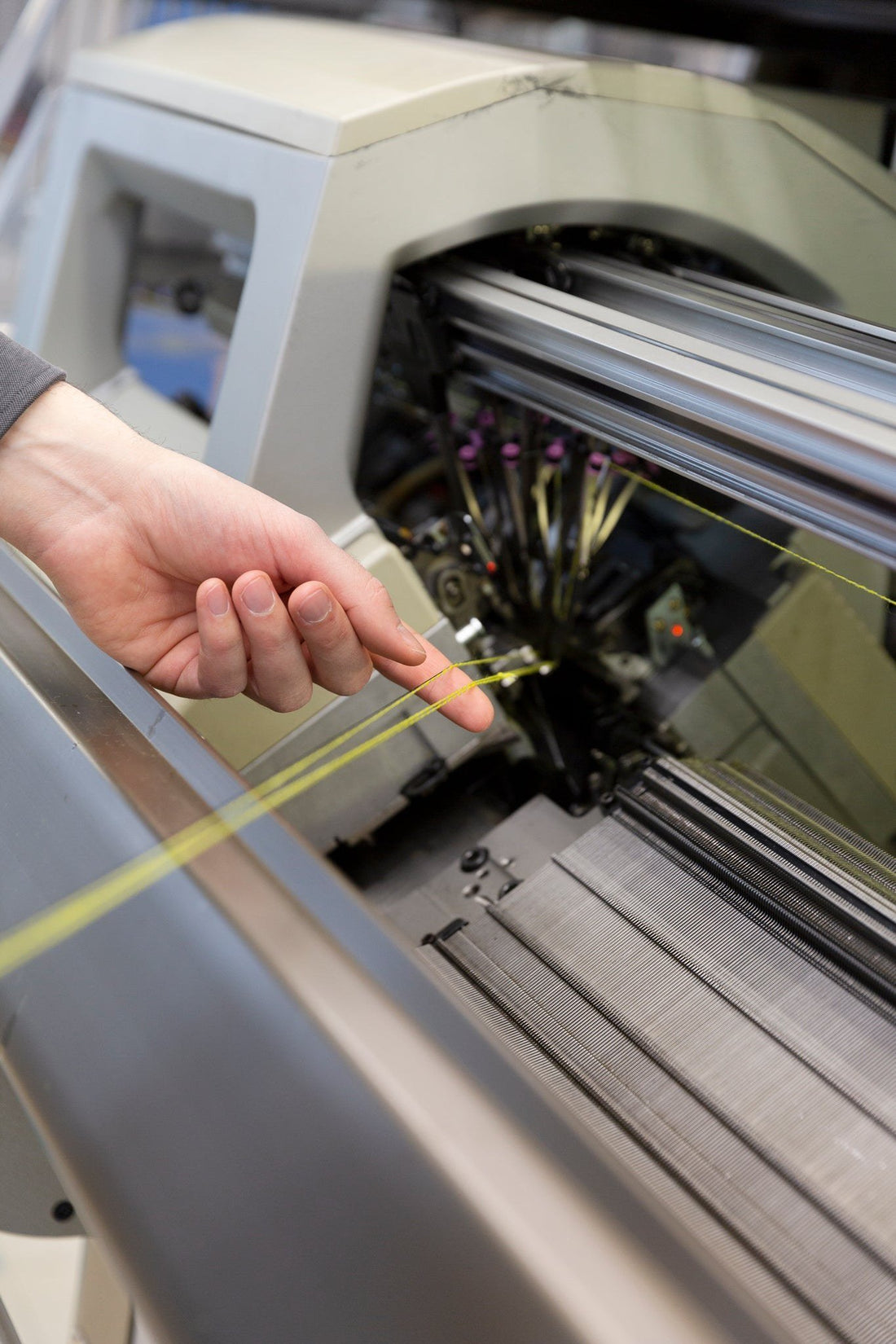 A hand guiding yellow yarn into a knitting machine at a factory in Austria.