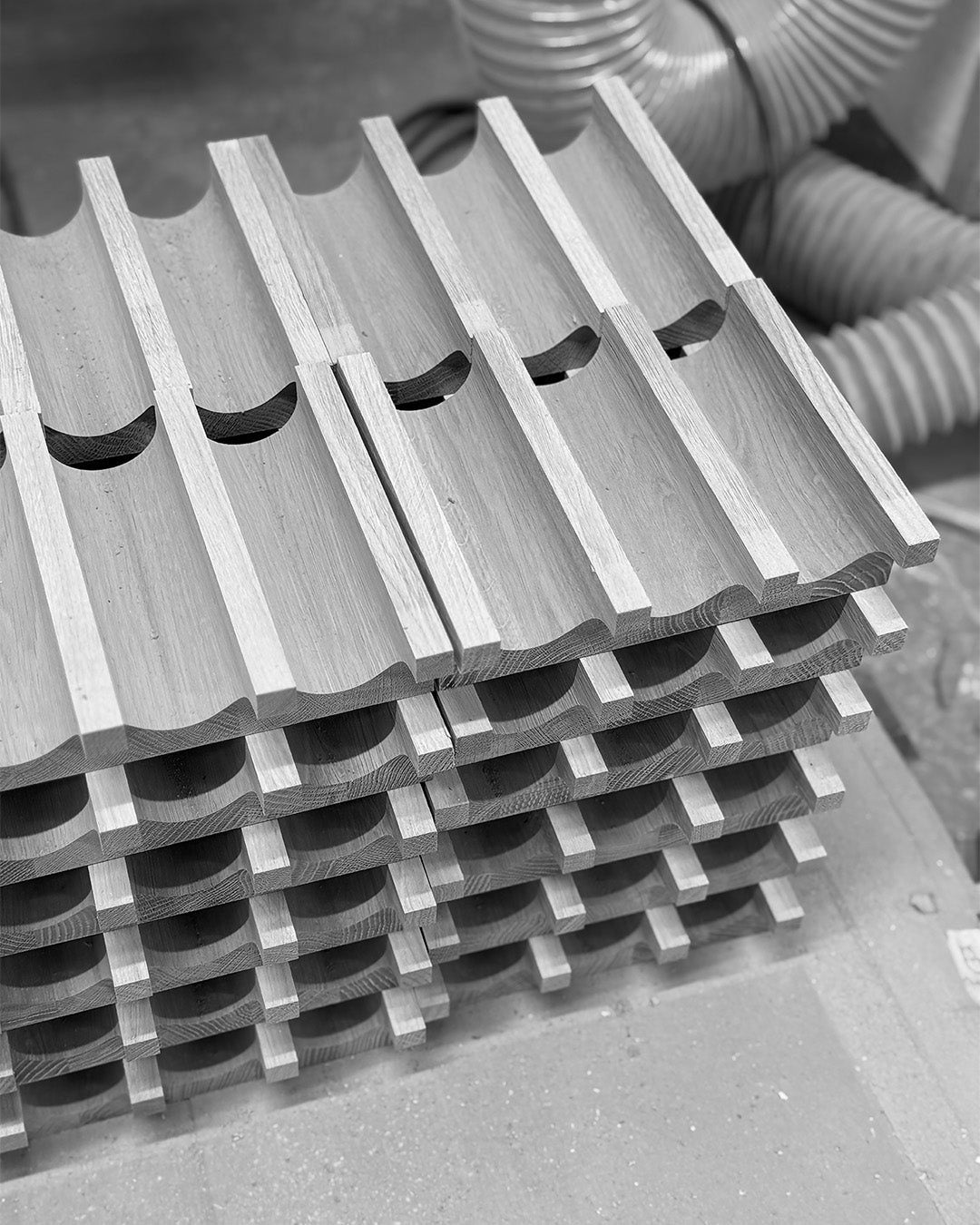 Freshly milled oak parts of the Column Coat Rack stacked in the workshop (black and white).