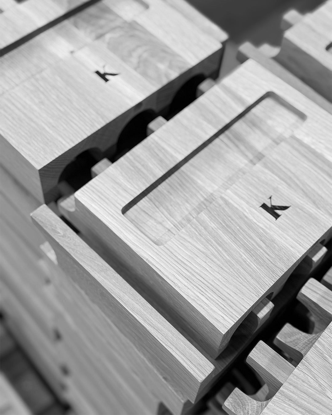 Close-up of stacked oak bases with a branded K logo in the workshop (black and white).