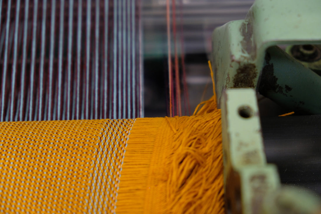 Close-up of a loom: warp threads and freshly woven ochre wool fabric with a fringed edge, Kvadrat's own production.