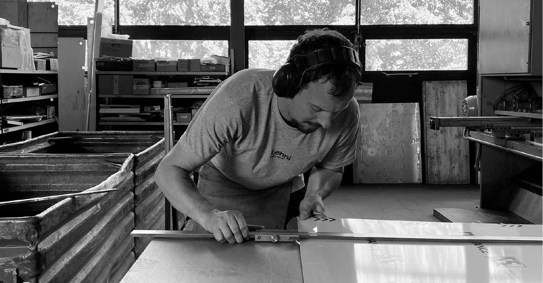 A metalworker wearing ear defenders aligns an aluminium sheet against a guide on the workbench.