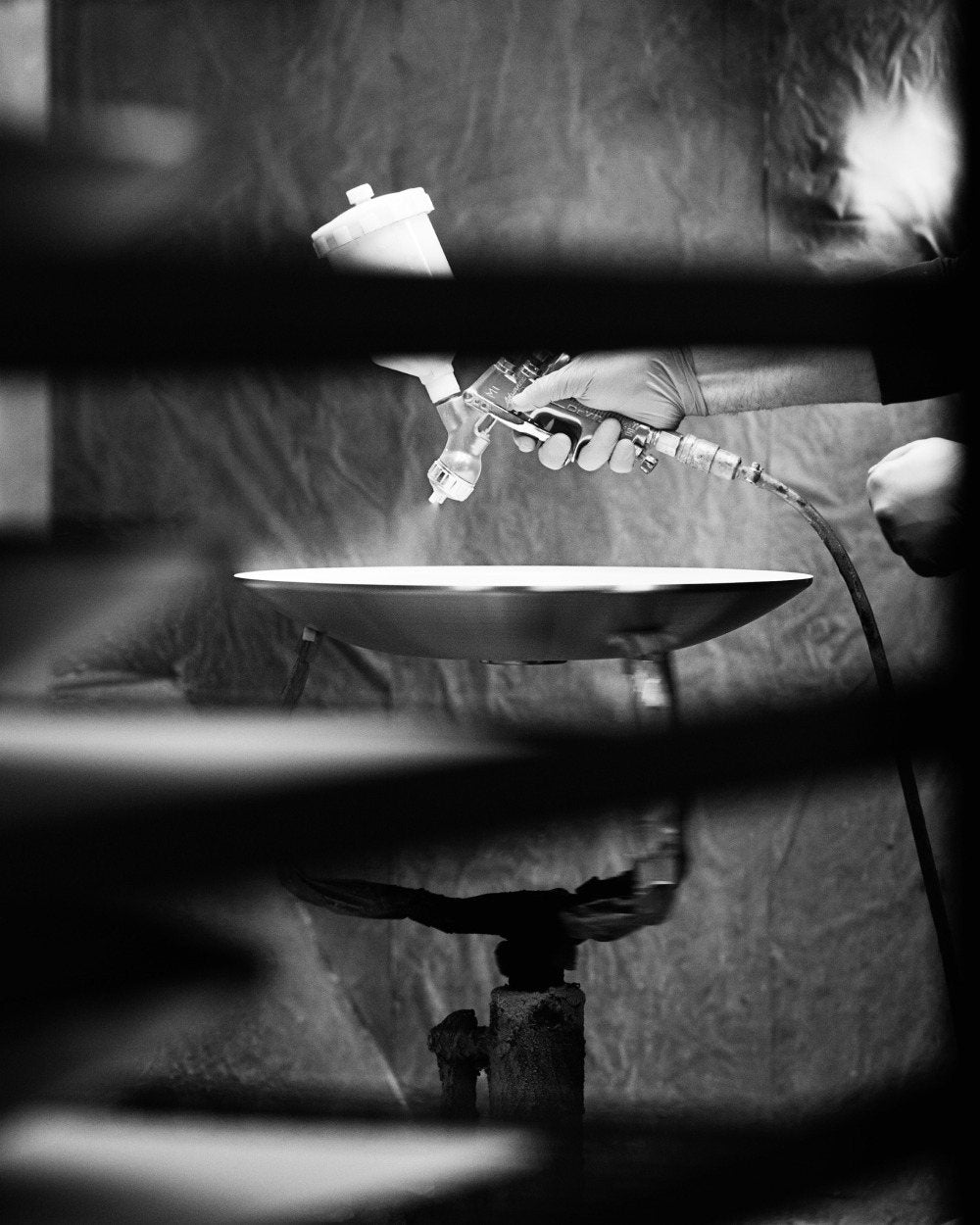 Black and white: hands with a spray gun paint a metal shade in the paint booth.