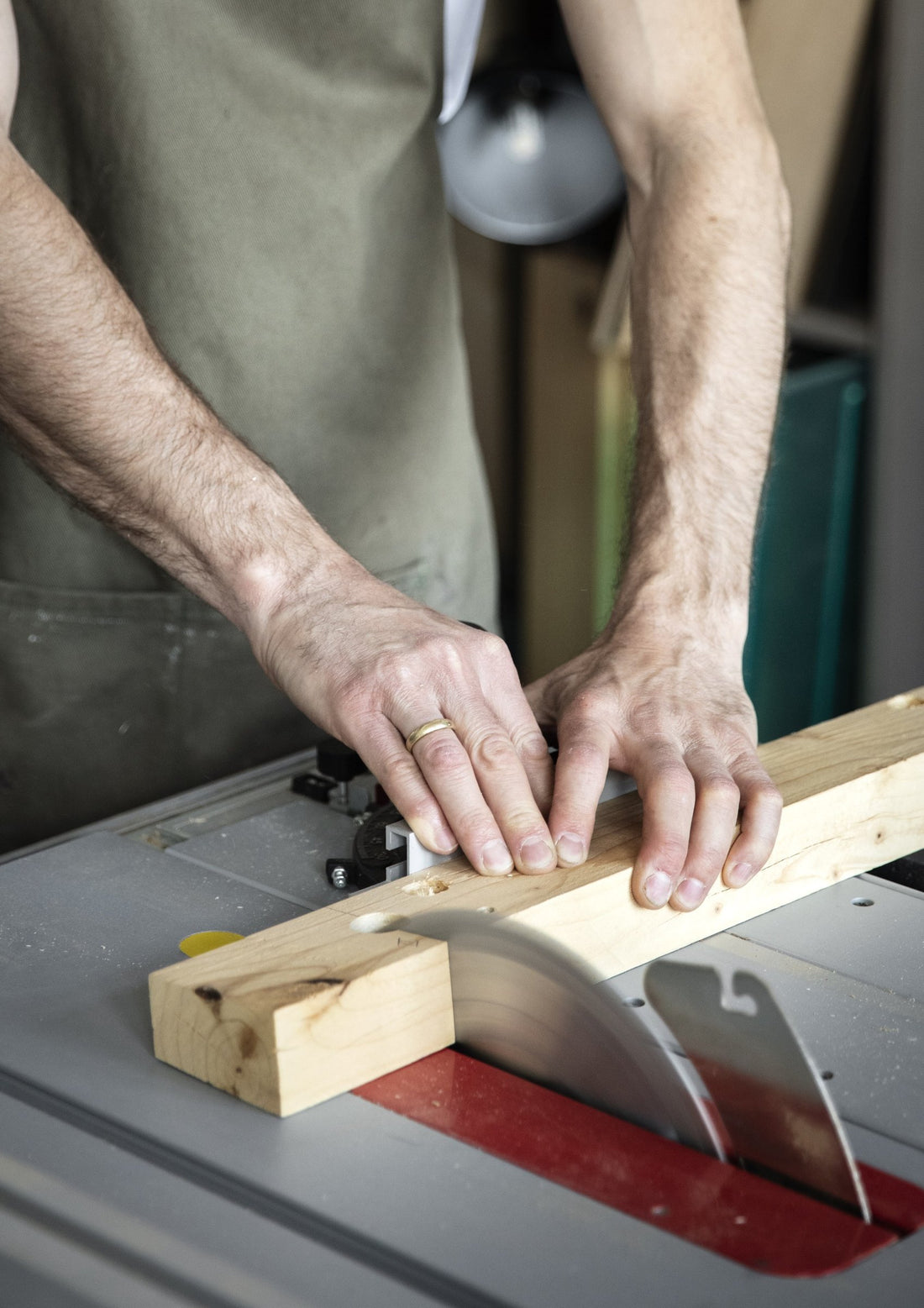Hands guiding a piece of solid wood across a table saw in the workshop.