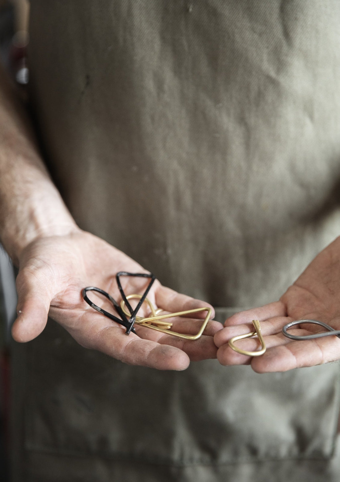 Open hands holding small bent brass and black metal parts in the workshop.