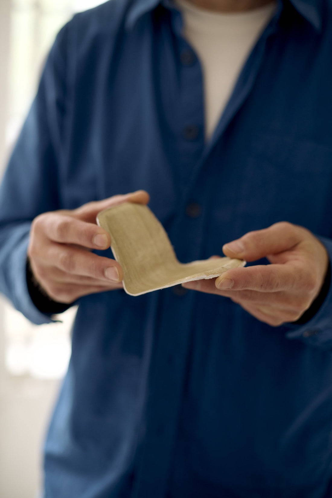 Hands holding a small plywood model of a chair seat during its development.