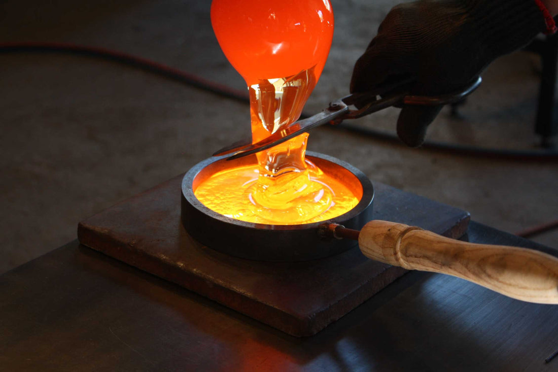 A glassmaker cuts off glowing glass with shears as it flows into a mould at Holmegaard Glasværk.