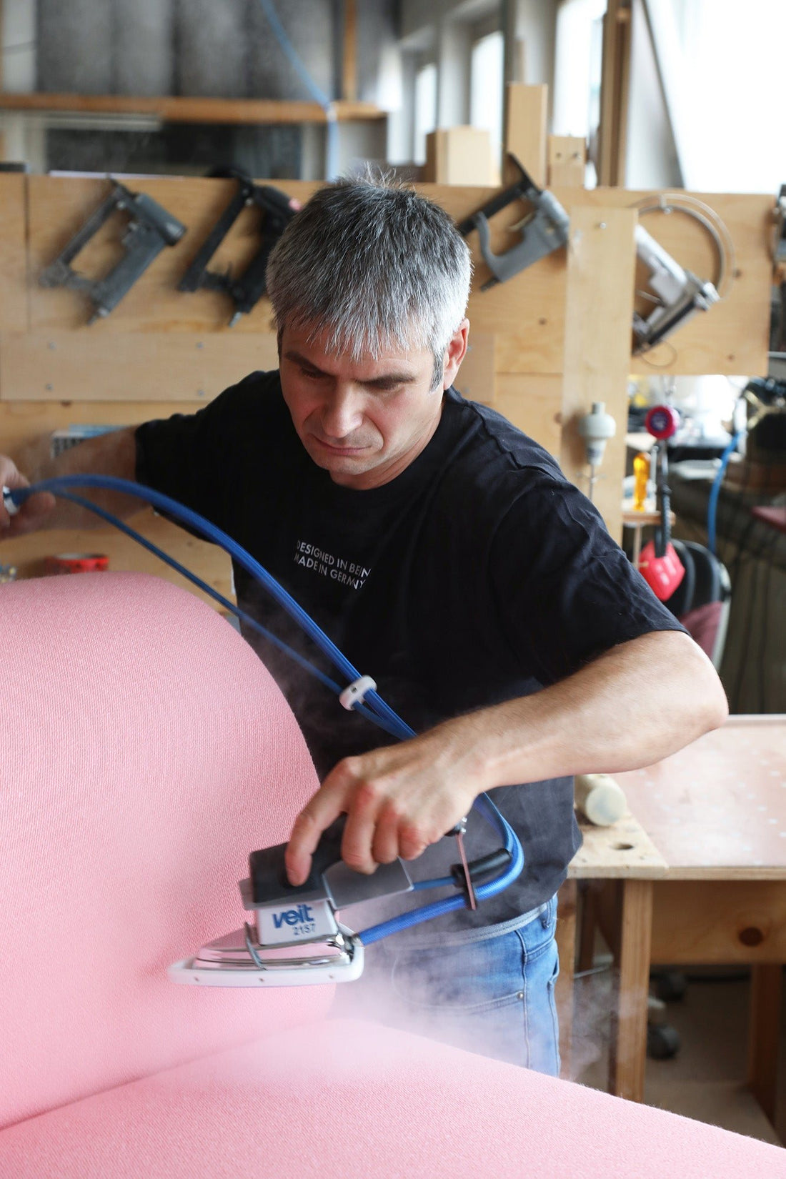 An upholsterer smooths the pink cover of an OUT sofa with a steam iron in the upholstery workshop.