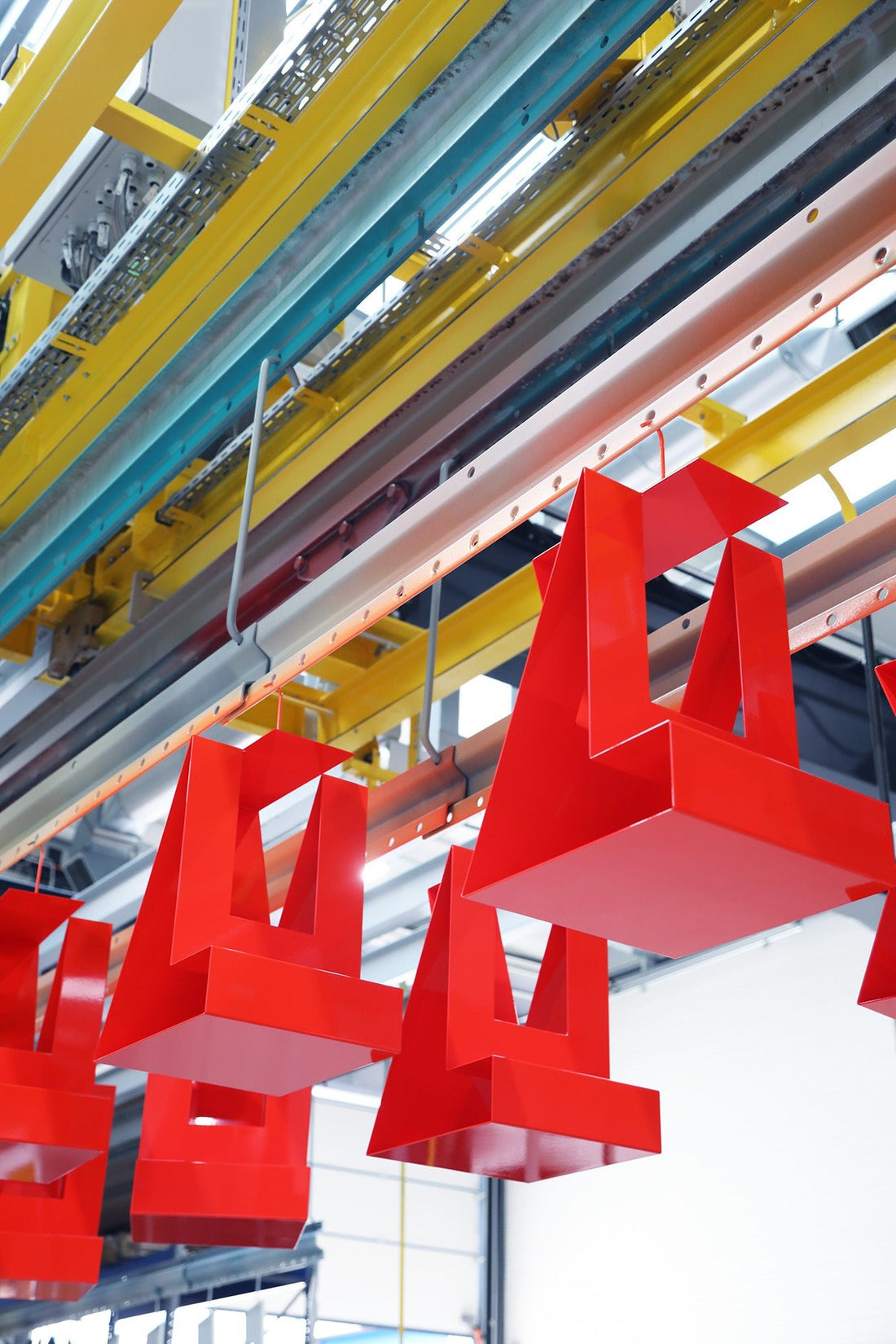 Freshly red powder-coated steel furniture by OUT hangs on the conveyor of the coating line.