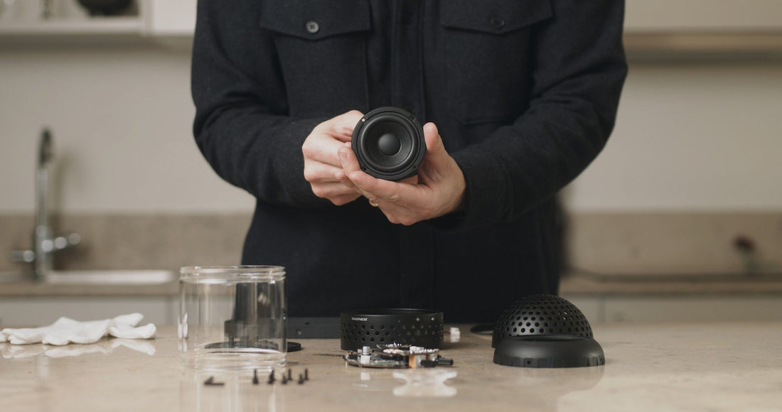Hands hold a speaker driver above the disassembled parts of a Light Speaker laid out on a workbench.