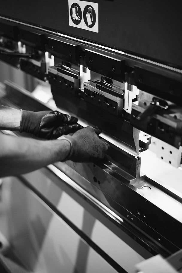 Gloved hands feed an aluminium sheet into a press brake during the making of UTIL's Plié pieces