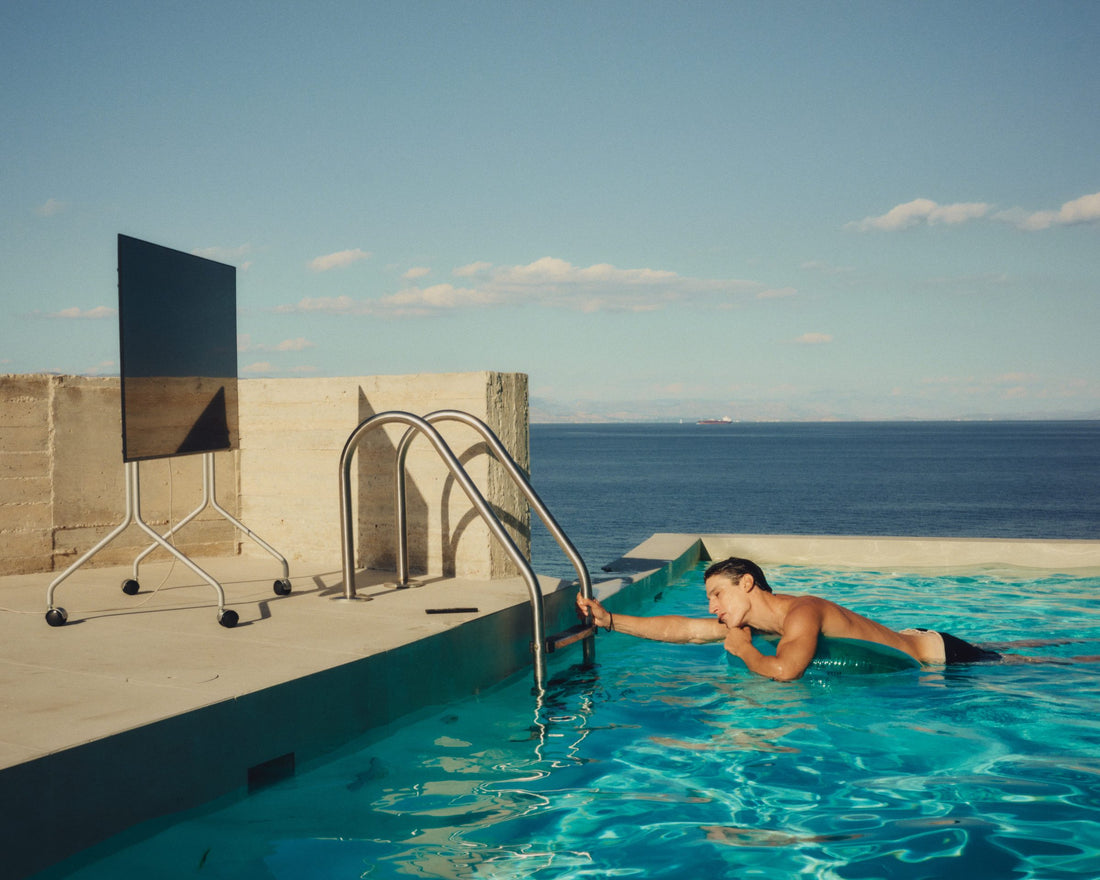 A Pedestal Moon TV stand on a concrete terrace beside a pool by the sea, a man in the water holding the pool ladder, still from Objects of Desire